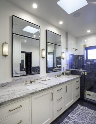 A bathroom with marble counter tops and a skylight.